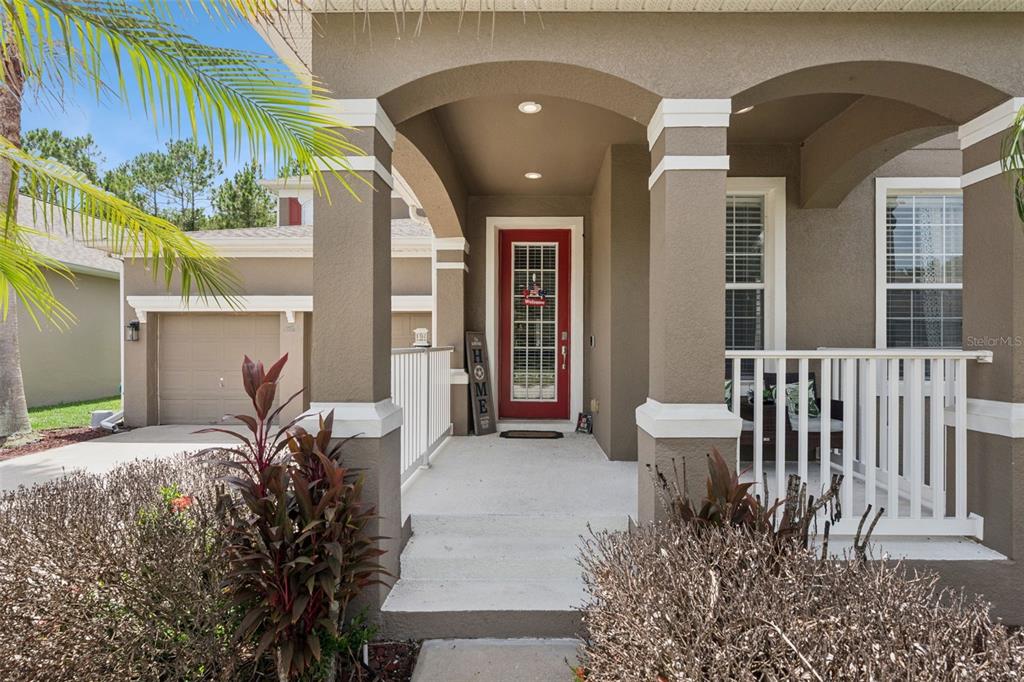 A tan house exterior features a covered front porch, white railings, and a red front door — 9528 PICCADILLY SKY WAY, ORLANDO, FL