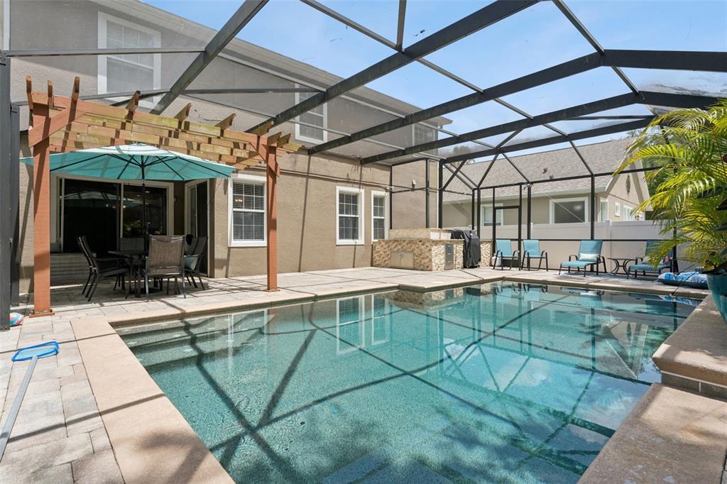 A screened-in patio features a swimming pool, a wooden pergola, and an outdoor kitchen — 9528 PICCADILLY SKY WAY, ORLANDO, FL