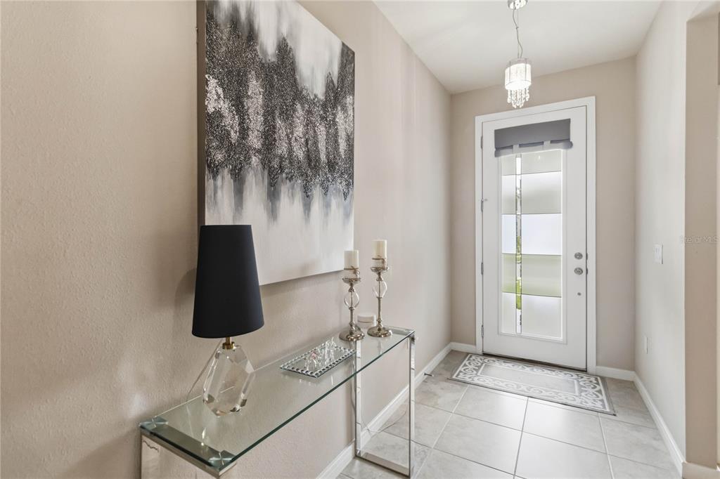 A modern entryway features a glass console table, abstract wall art, and a glass-paneled door — 5179 ROYAL POINT AVENUE, KISSIMMEE, FL