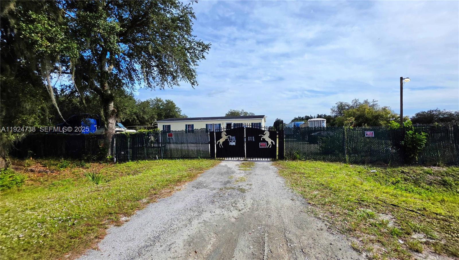 A gravel driveway leads to a gated entrance in front of a single-story house — 225 N Estribo ST, Clewiston FL 33440, CLEWISTON, FL