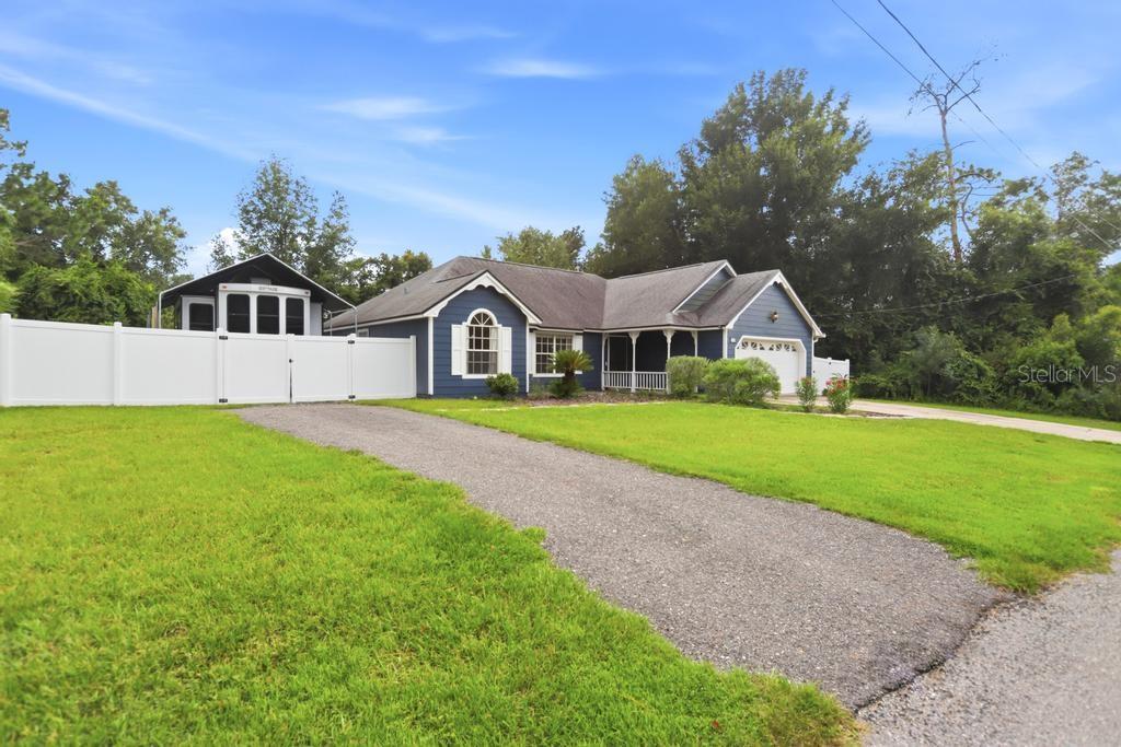 A blue single-story house with a gravel driveway and a white vinyl fence — 1714 20TH STREET, ORANGE CITY, FL