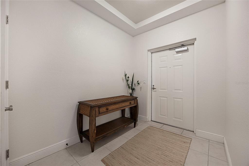 An entryway features white walls, tile flooring, a wooden console table, and a white door — 14041 BELLAGIO WAY UNIT 214, OSPREY, FL