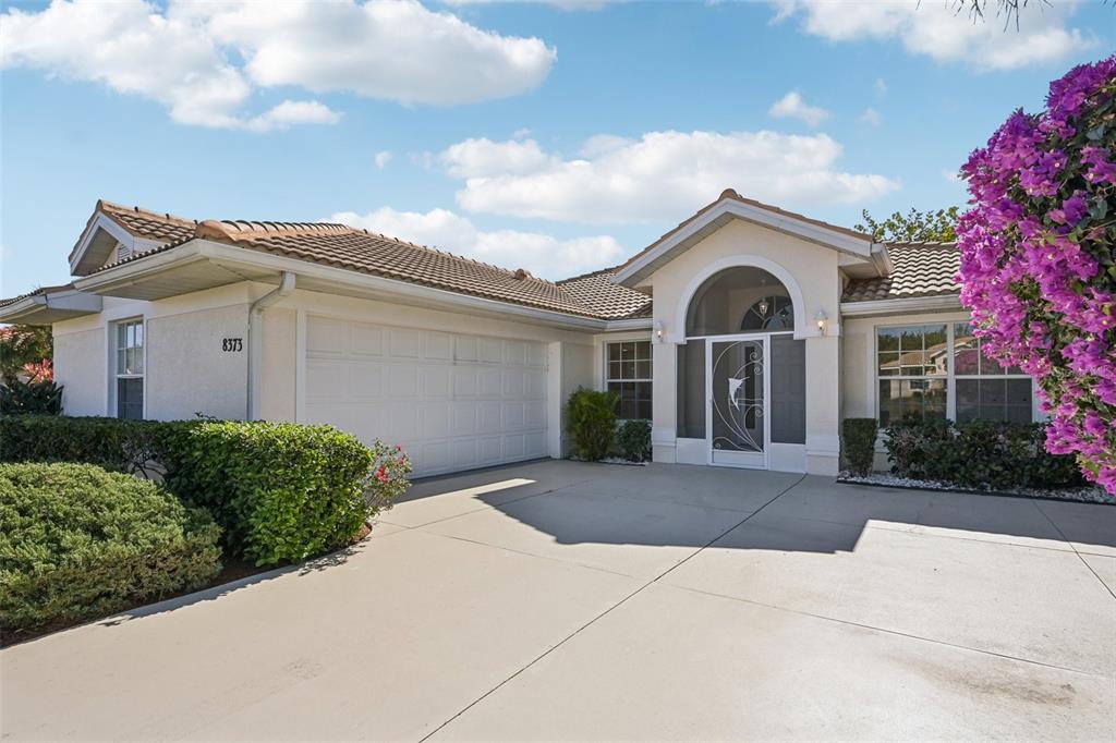 A single-story house with a white garage, arched entryway, and a large purple bougainvillea bush — 8373 PONDVIEW LANE, ENGLEWOOD, FL