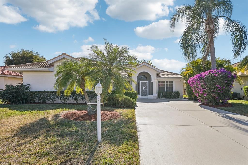A single-story house with a concrete driveway, palm trees, and a purple flowering bush — 8373 PONDVIEW LANE, ENGLEWOOD, FL