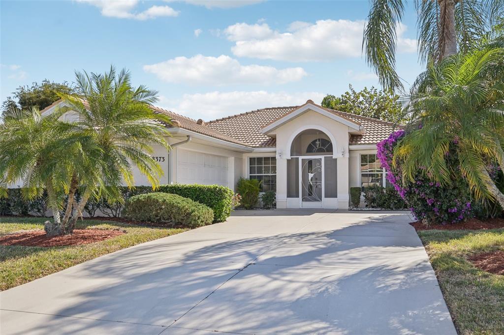 A single-story house with a beige stucco exterior, a tiled roof, and a concrete driveway — 8373 PONDVIEW LANE, ENGLEWOOD, FL