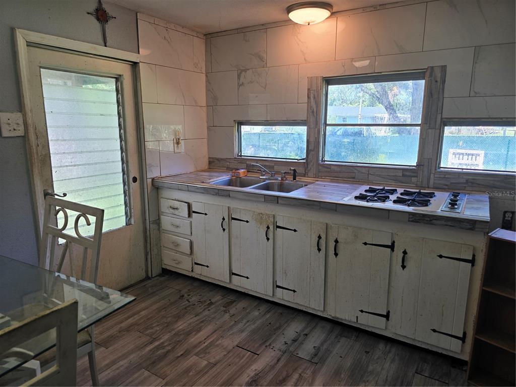 A kitchen features white cabinets, a drop-in cooktop, a double sink, and marble-look wall tiles — 5302 SWAYING PALM DRIVE, PUNTA GORDA, FL