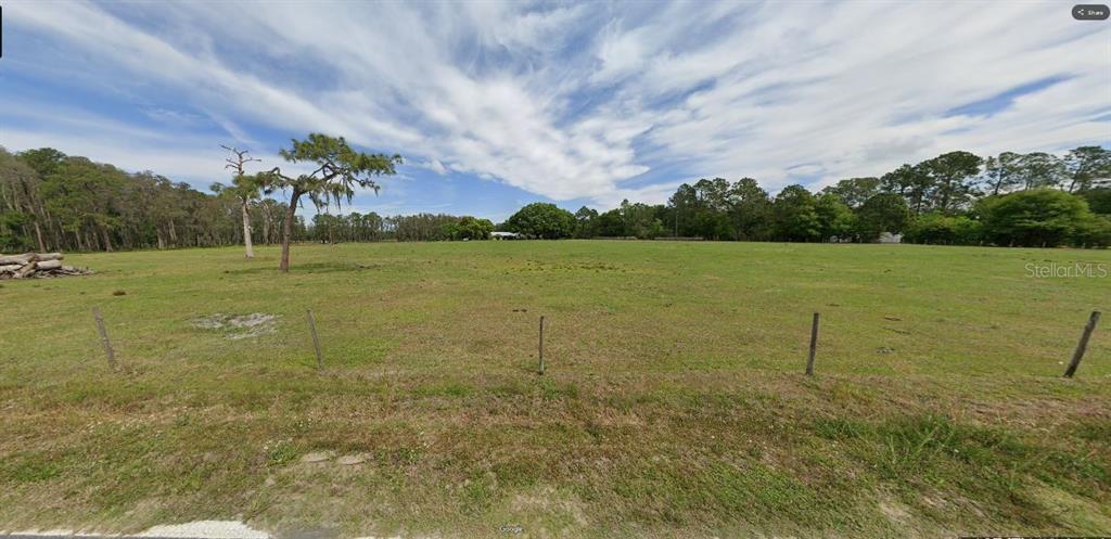 A wide, grassy, fenced-in field with scattered trees under a blue sky with wispy clouds — GREEN POND RD, POLK CITY, FL