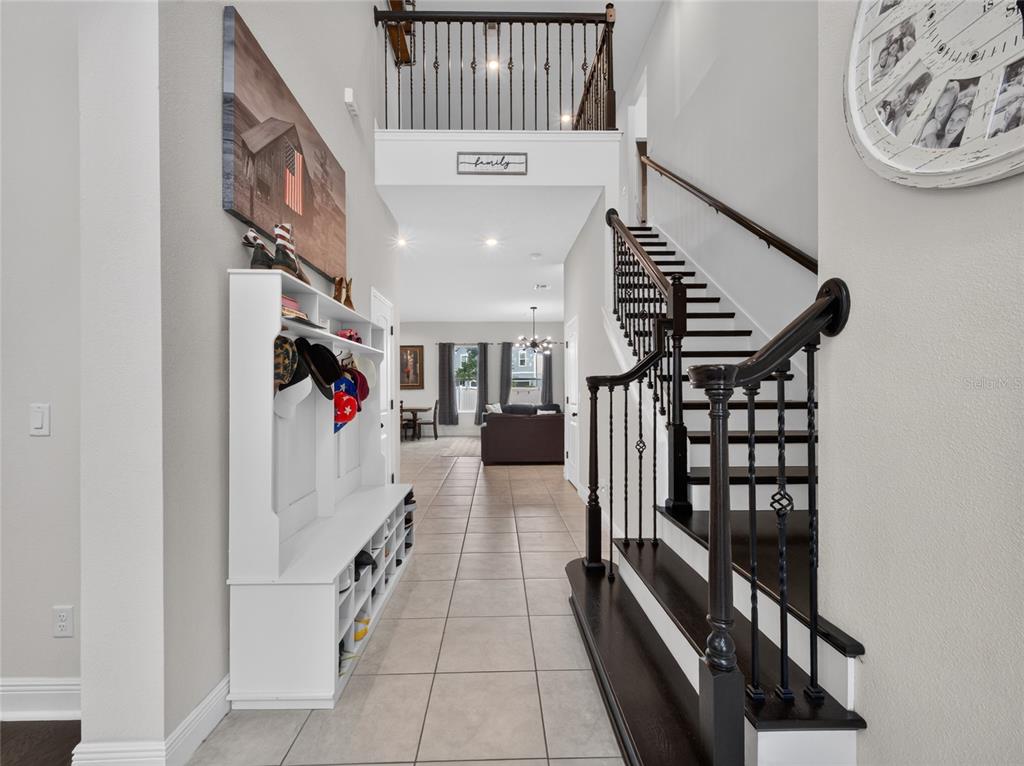 A bright entryway features a white mudroom bench, tile flooring, and a dark wood staircase — 659 RED HAVEN LANE, OVIEDO, FL