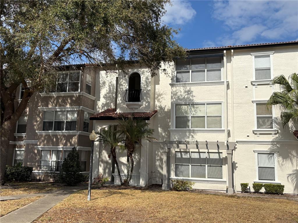 A three-story apartment building features beige stucco walls, a tiled roof, and a small balcony — 5152 CONROY ROAD UNIT 1316, ORLANDO, FL