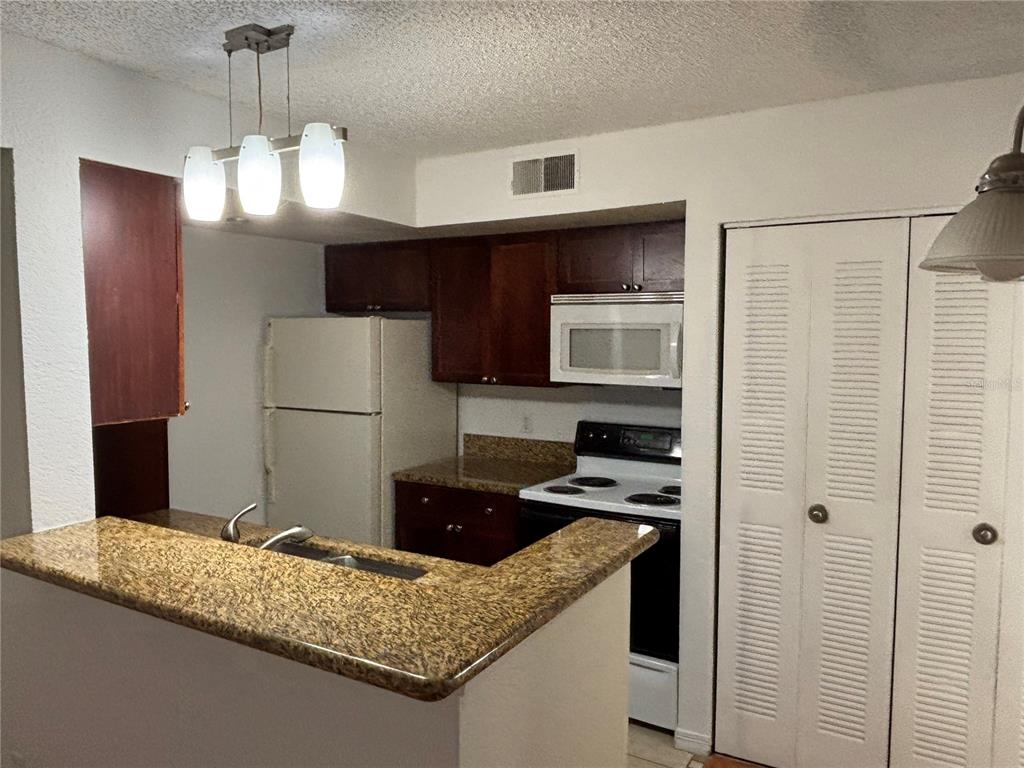 A kitchen features dark wood cabinets, granite countertops, white appliances, and a breakfast bar — 5152 CONROY ROAD UNIT 1316, ORLANDO, FL