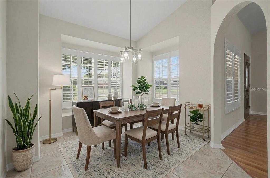 A dining room features a wooden table, upholstered chairs, a chandelier, and plantation shutters — 6208 HUNTINGTON DRIVE, ZEPHYRHILLS, FL