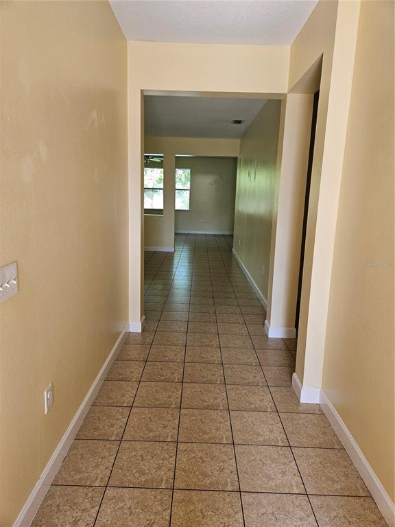 A hallway with tan tile flooring leads into an open living area with large windows — 5013 BALLARK STREET, MOUNT DORA, FL