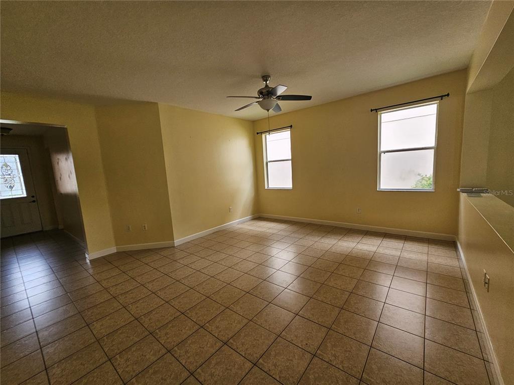 An empty room with yellow walls, tile flooring, a ceiling fan, and two windows — 5013 BALLARK STREET, MOUNT DORA, FL