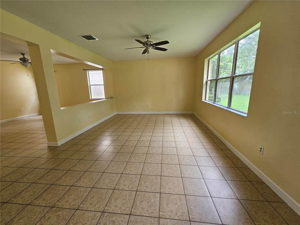 A spacious room with beige tile flooring, yellow walls, a ceiling fan, and large windows — 5013 BALLARK STREET, MOUNT DORA, FL