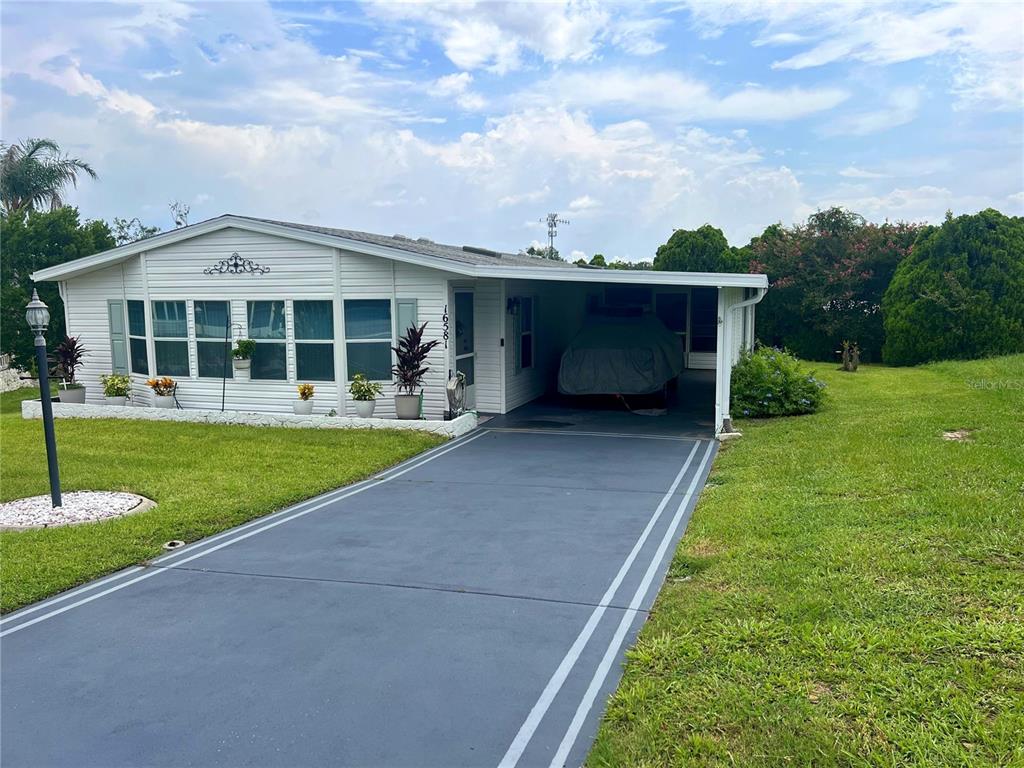 A single-story manufactured home features white siding, a covered carport, and a paved driveway — 16581 SE 96TH AVENUE, SUMMERFIELD, FL