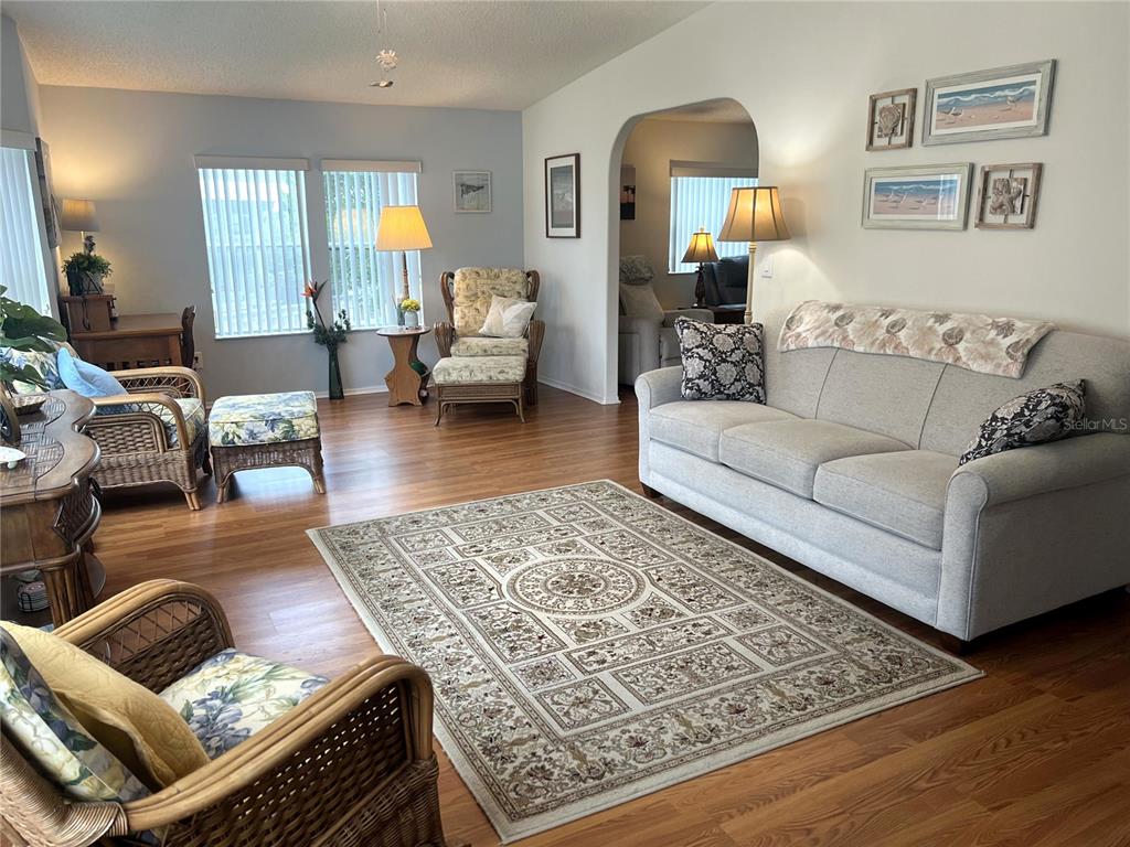 A living room features a light gray sofa, wicker chairs, and an area rug on wood flooring — 16581 SE 96TH AVENUE, SUMMERFIELD, FL