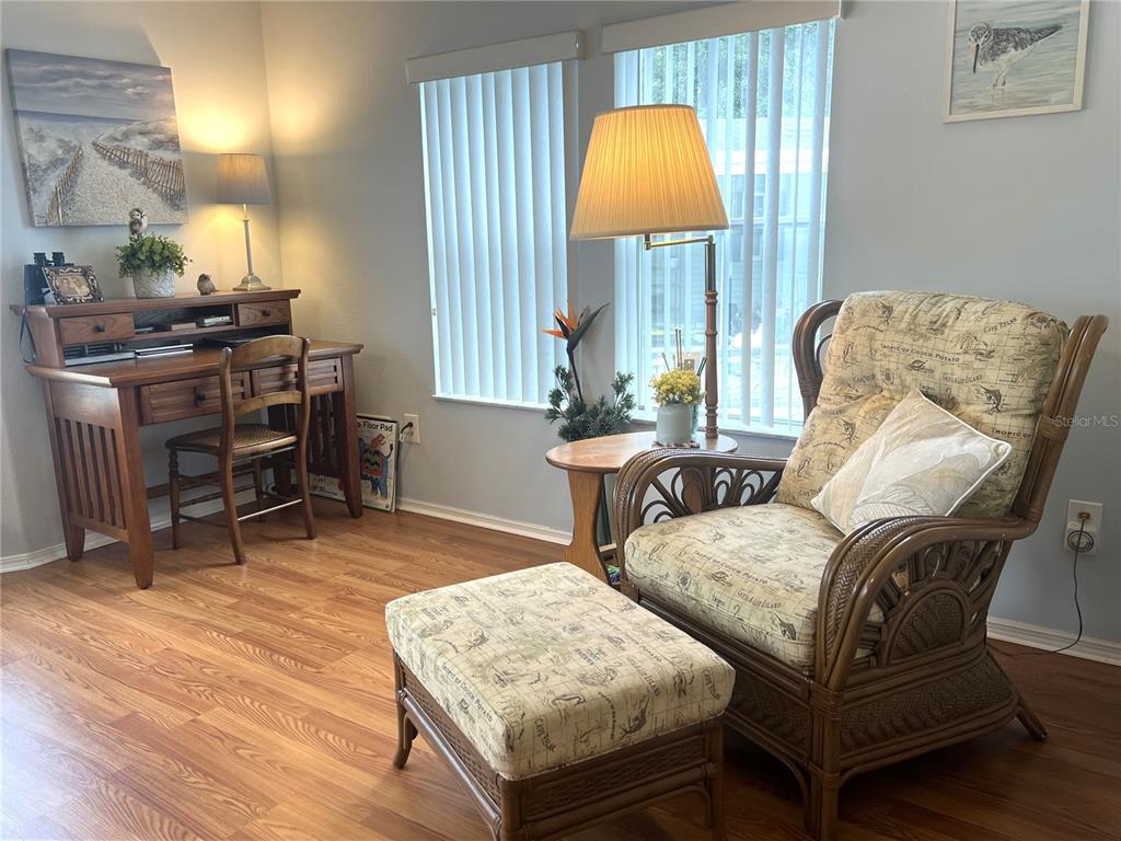 A room features a wooden desk, a wicker armchair with an ottoman, and vertical blinds — 16581 SE 96TH AVENUE, SUMMERFIELD, FL