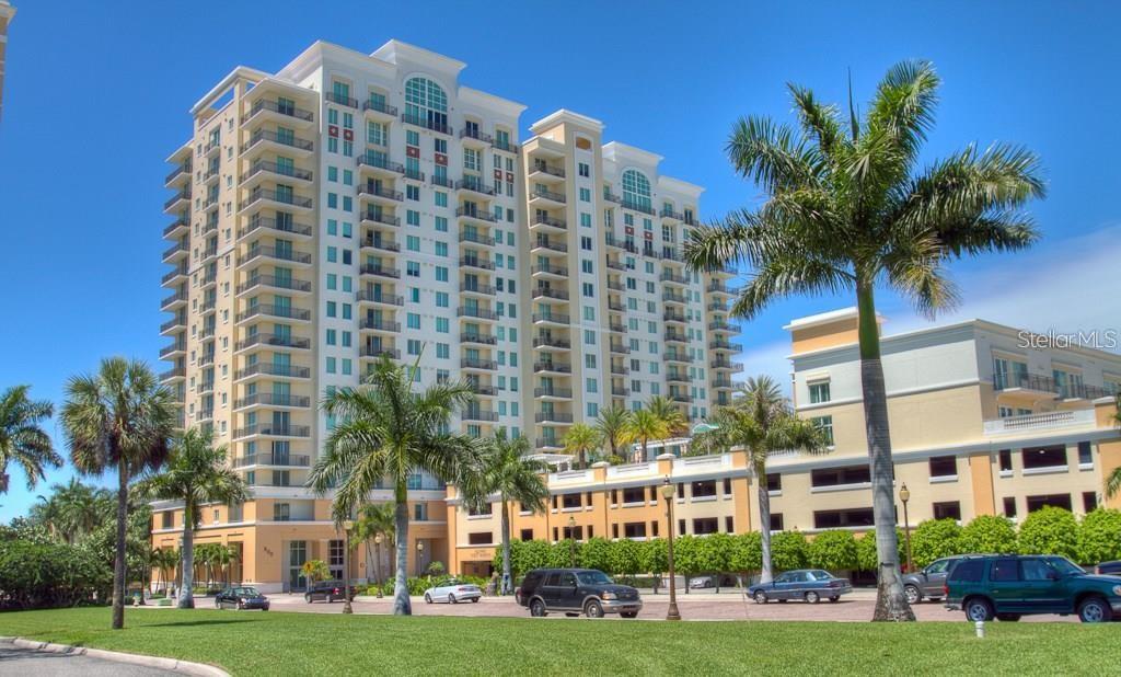 A tall, multi-story residential building with balconies stands behind a parking lot and palm trees — 800 N TAMIAMI TRAIL UNIT 905, SARASOTA, FL