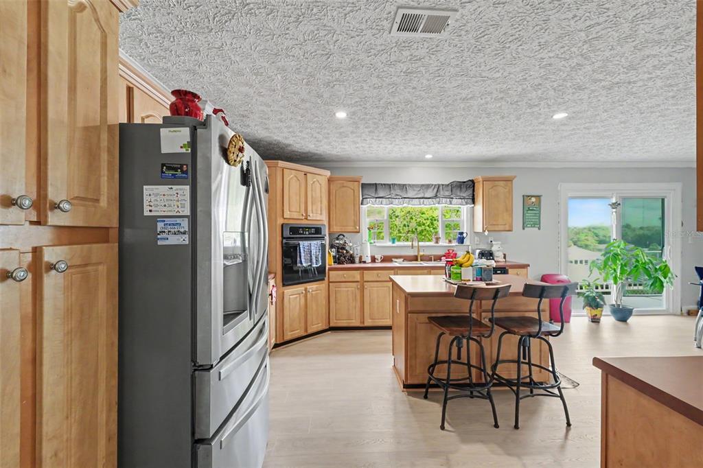 A kitchen with light wood cabinets, a center island with stools, and a stainless refrigerator — 8043 TOWER STREET, BROOKSVILLE, FL