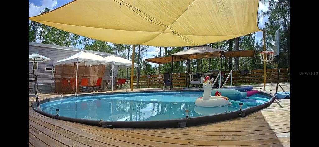 An above-ground swimming pool with a large shade sail sits on a wooden deck — 5590 W X ANNE LANE, DUNNELLON, FL