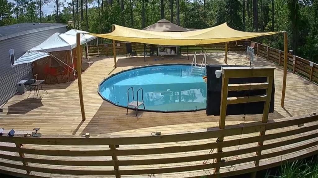 An elevated wooden deck surrounds an above-ground swimming pool with a large yellow shade sail — 5590 W X ANNE LANE, DUNNELLON, FL