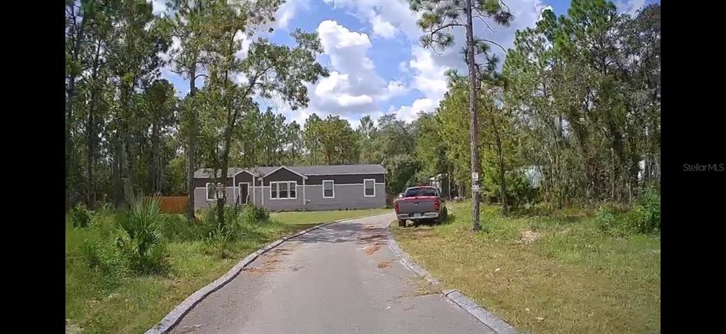A gray manufactured home sits at the end of a paved driveway surrounded by trees — 5590 W X ANNE LANE, DUNNELLON, FL
