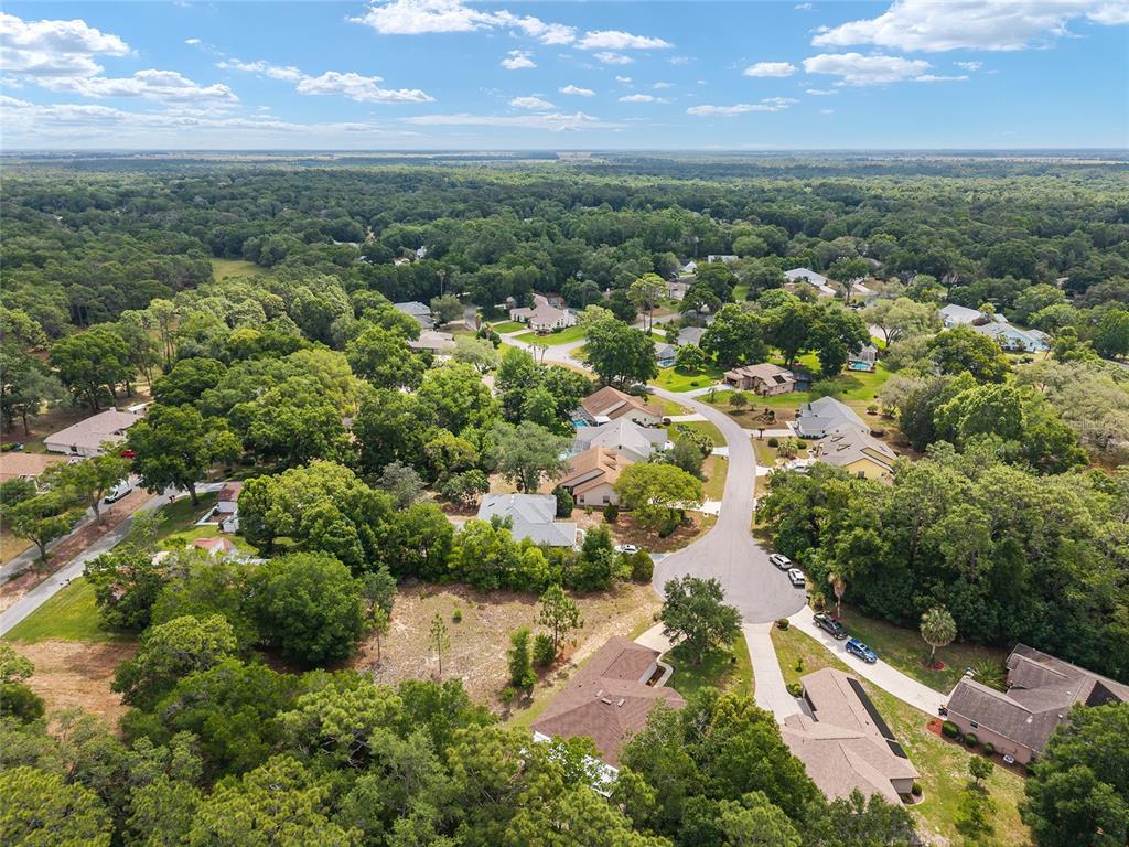 An aerial view shows a suburban neighborhood with houses nestled among dense trees — 19939 SW 93RD LANE, DUNNELLON, FL