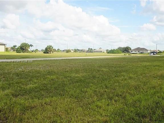 A large, flat, grassy vacant lot sits in front of a paved road and suburban houses — 4500 NW 34th Ter, Cape Coral FL 33993, CAPE CORAL, FL