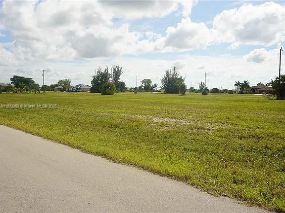 A large, flat, grassy vacant lot is bordered by an asphalt road under a cloudy sky — 4500 NW 34th Ter, Cape Coral FL 33993, CAPE CORAL, FL
