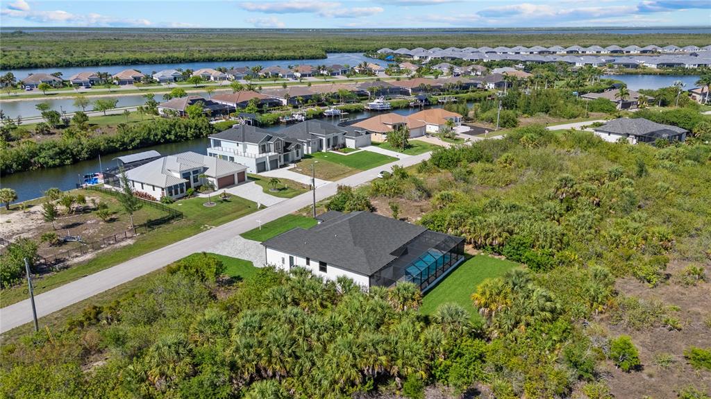 An aerial view shows a residential neighborhood with houses, canals, and surrounding natural vegetation — 15101 LEIPZIG CIRCLE, PORT CHARLOTTE, FL