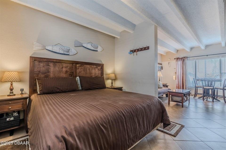A bedroom features a large bed, tiled floors, and an adjacent seating area — 935 S ATLANTIC AVENUE UNIT 128, DAYTONA BEACH, FL