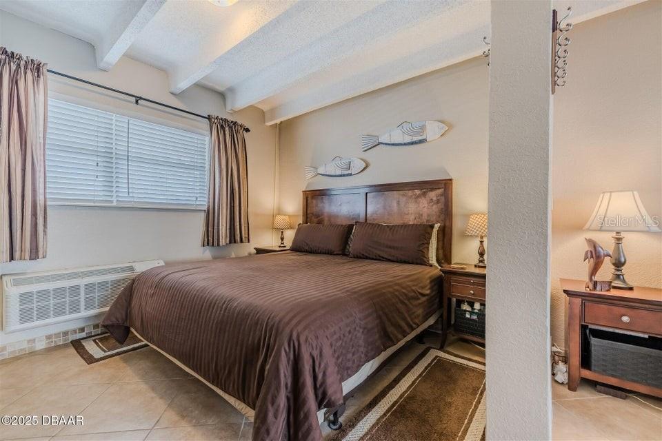 A bedroom features a queen bed, wood headboard, tile floors, and coastal wall decor — 935 S ATLANTIC AVENUE UNIT 128, DAYTONA BEACH, FL