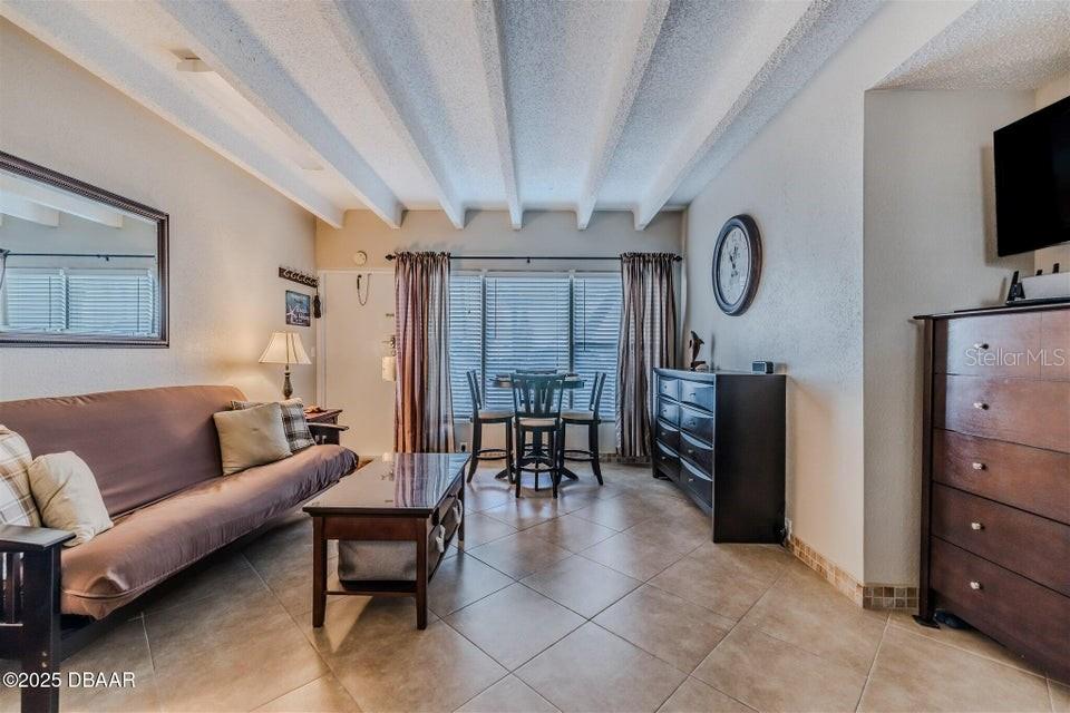 A living room features tile flooring, a brown sofa, a dining set, and exposed ceiling beams — 935 S ATLANTIC AVENUE UNIT 128, DAYTONA BEACH, FL