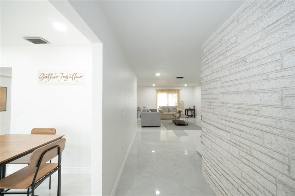 A view from a dining area looking toward a living room with white stone walls — 8413 MILLWOOD DRIVE, TAMPA, FL