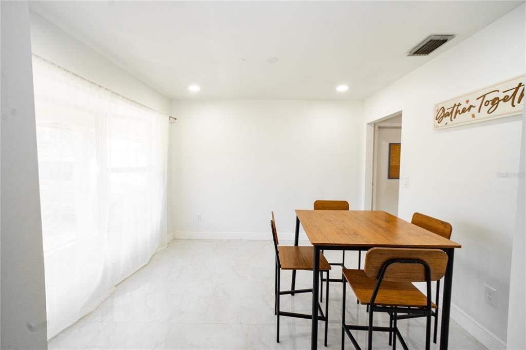 A dining area features a wooden table with four chairs, white walls, and light-colored tile flooring — 8413 MILLWOOD DRIVE, TAMPA, FL