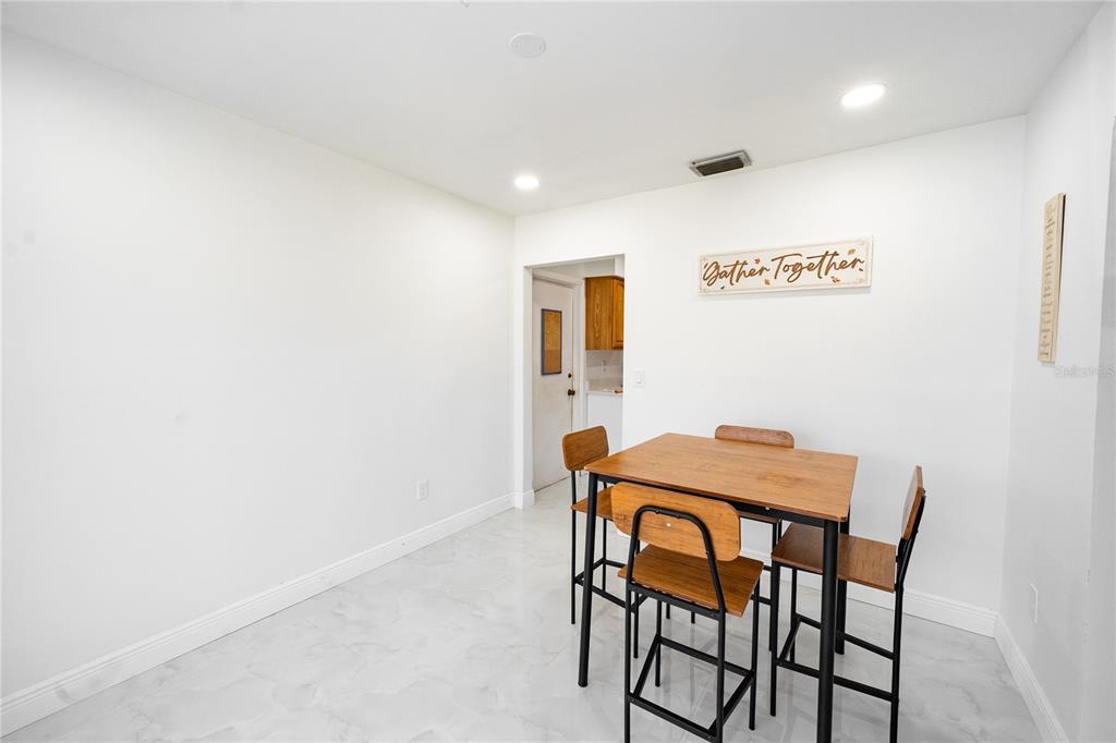 A dining area features a square wooden table with four chairs on a light floor — 8413 MILLWOOD DRIVE, TAMPA, FL