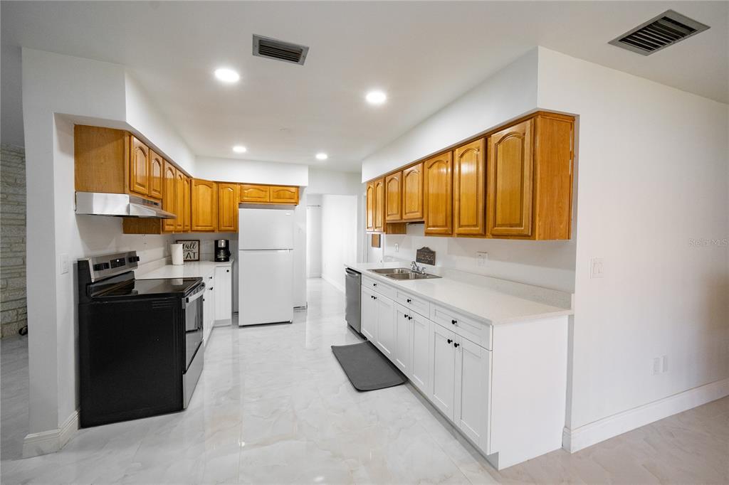 A kitchen features white lower cabinets, wood upper cabinets, white countertops, and a black stove — 8413 MILLWOOD DRIVE, TAMPA, FL