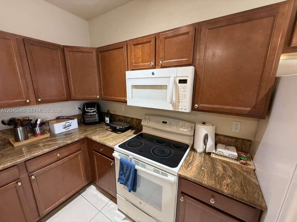 A kitchen features brown wooden cabinets, granite countertops, and a white electric range — 9572 SW 169th Pl, Miami FL 33196, MIAMI, FL