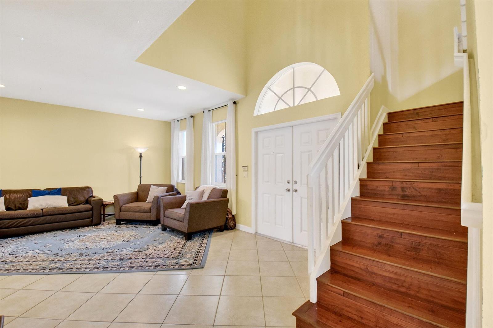A living room with tile floors, a wooden staircase, and a double-door entryway — 10624 Old Hammock Way, Wellington FL 33414, WELLINGTON, FL