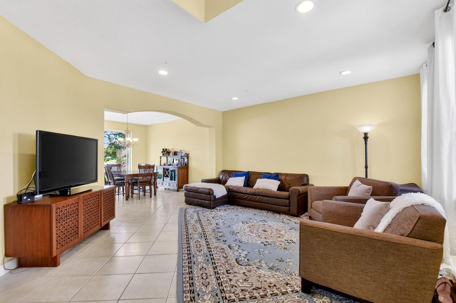 A living room with tile floors, a brown sectional, and a dining area visible beyond — 10624 Old Hammock Way, Wellington FL 33414, WELLINGTON, FL