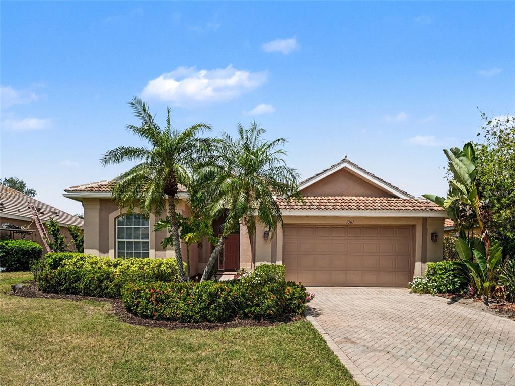 A single-story house with a tan stucco exterior, a tiled roof, and a paved driveway — 1361 NEW FOREST LANE, OSPREY, FL