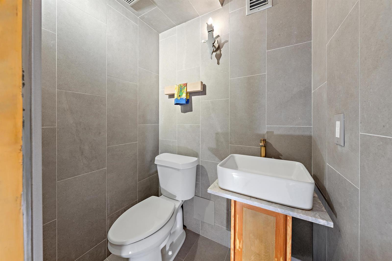A small bathroom features gray tiled walls, a white toilet, and a vessel sink vanity — 1516 S Lakeside Drive # 106, FL 33460, FL