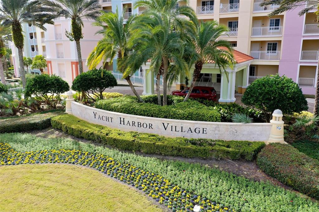 An exterior view of the Yacht Harbor Village entrance sign with palm trees and buildings — 237 and 239 YACHT HARBOR DR, PALM COAST, FL