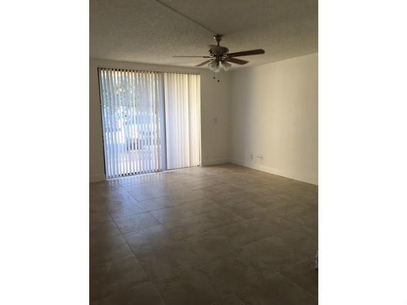 An empty living room features large beige floor tiles, a ceiling fan, and vertical blinds — 4003 N University Drive # 107, Sunrise FL 33351, SUNRISE, FL