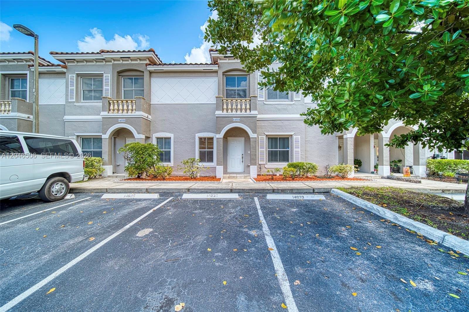A two-story townhouse exterior features a white front door, arched entryway, and dedicated parking spaces — 14033 SW 49th St # 6, Miramar FL 33027, MIRAMAR, FL