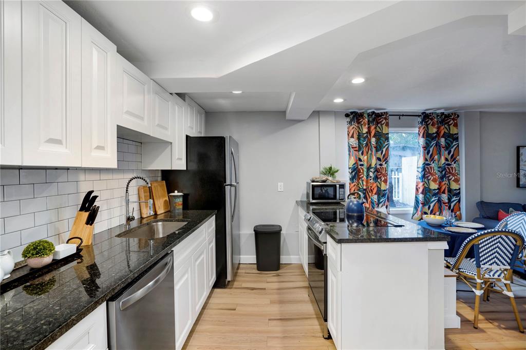 A kitchen features white cabinets, black granite countertops, stainless steel appliances, and wood-look flooring — 4705 HOLLINGSWORTH AVENUE UNIT Lower, SARASOTA, FL