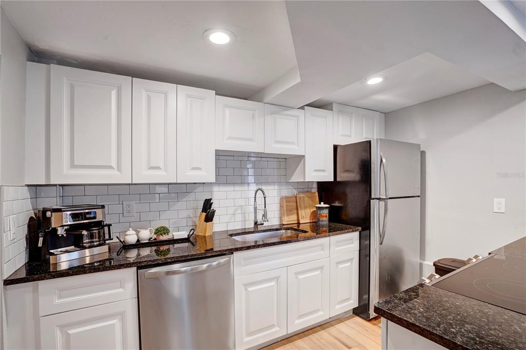 A kitchen features white cabinets, dark granite countertops, stainless steel appliances, and a subway tile backsplash — 4705 HOLLINGSWORTH AVENUE UNIT Lower, SARASOTA, FL