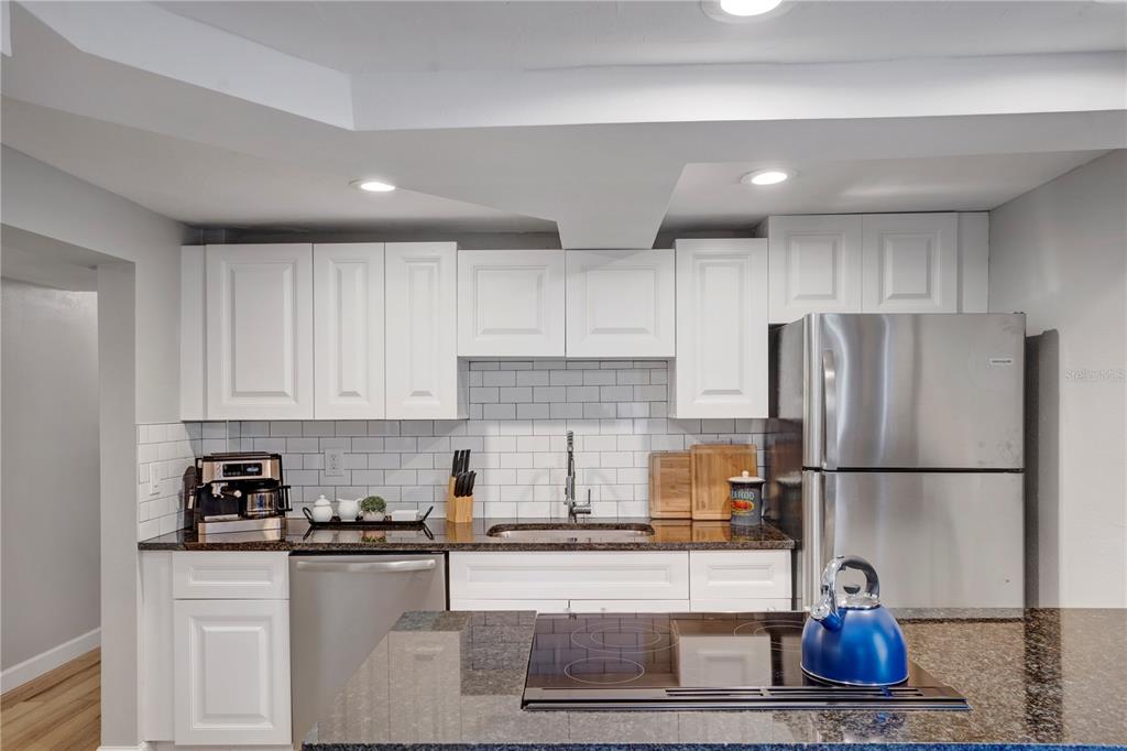 A kitchen features white cabinets, dark granite countertops, stainless steel appliances, and a subway tile backsplash — 4705 HOLLINGSWORTH AVENUE UNIT Lower, SARASOTA, FL