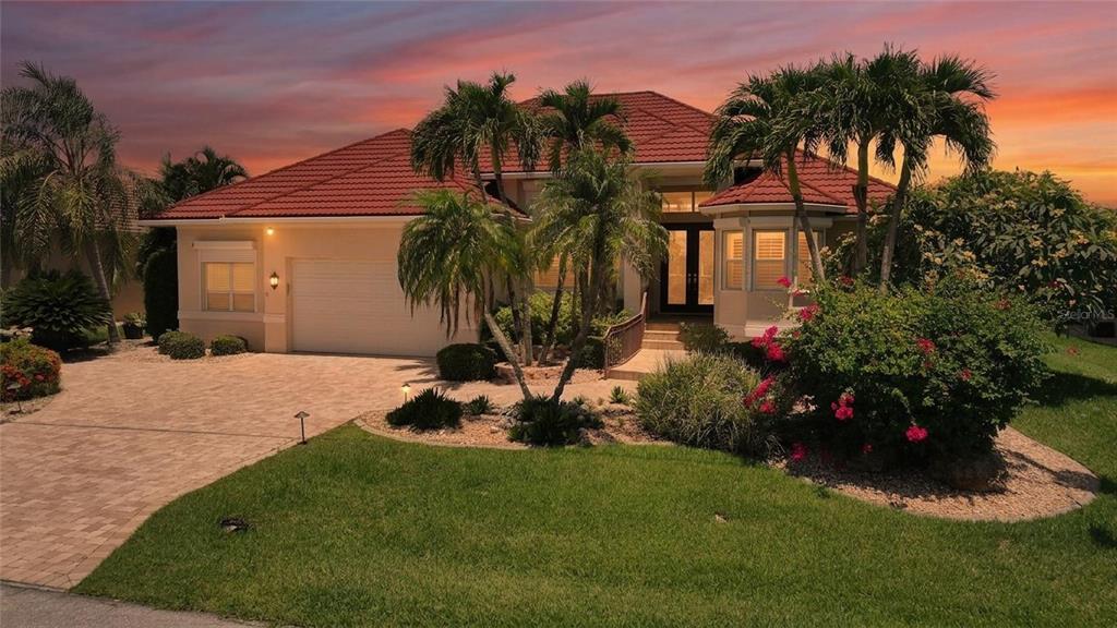 A single-story house with a red tile roof, a paved driveway, and tropical landscaping at sunset — 436 VALLETTA COURT, PUNTA GORDA, FL