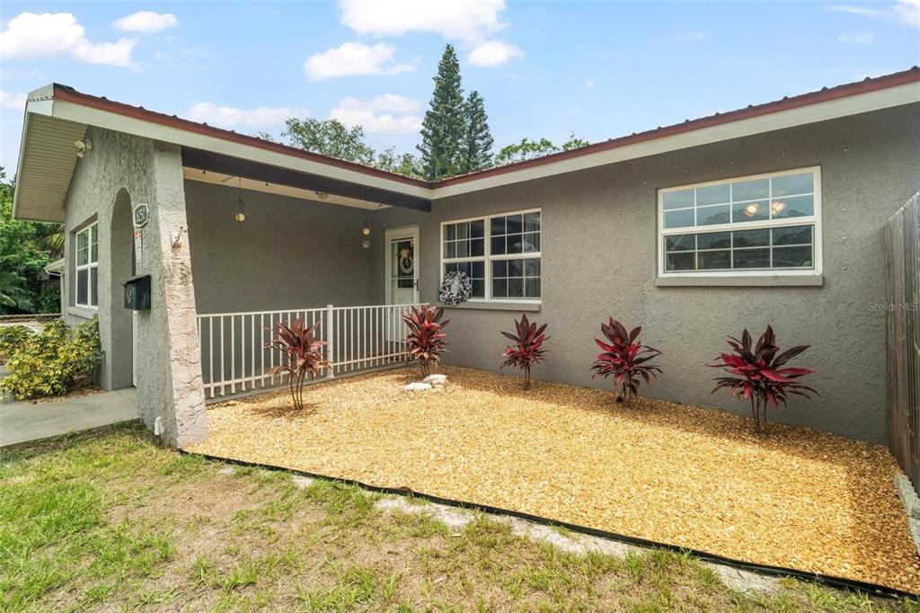 A gray house exterior features a covered porch, white railings, and a gravel front yard — 6250 5TH AVENUE S, ST PETERSBURG, FL